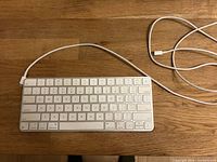 Full view of Apple Magic Keyboard with attached Lightning cable on wooden surface