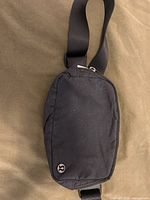 Front view of black Lululemon belt bag showing logo badge and zipper