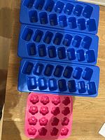 Group view of three blue plastic ice cube trays and one pink silicone flower mold tray