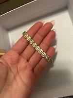 Bracelet in hand showing smiley-face links with green crystals