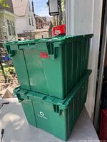 Two green plastic totes stacked, showing folding lids and overall condition