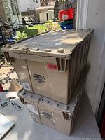 Two stacked beige plastic totes with folding lids, side graphics visible