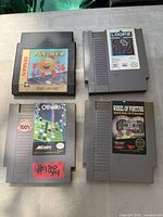 Four NES cartridges: Pac-Man, Loopz, Othello, Wheel of Fortune displayed on table