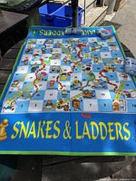 Overall view of Snakes and Ladders vinyl mat laid out on table with two rolled inflatable dice visible