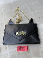 Front view of black Batman clutch showing bat ears, gold-tone logo clasp and chain