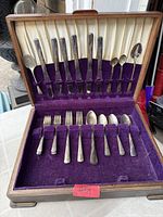 Open wood case showing arrangement of knives, forks, spoons, and serving pieces in purple felt interior