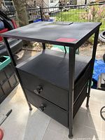Full view of black metal end table with charging panel on top, drawers, purple feet