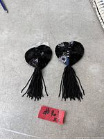 Top view of both black sequin heart pasties with tassels