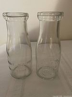 Front view of both glass milk bottles showing embossing and overall shape