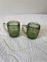 Front view of both green glass miniature barrel mugs