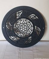 Front view of entire round grate showing ornate pattern and lettering