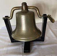 Front view of brass bell in black metal stand