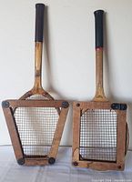 Front view of both wooden tennis rackets inside their triangular wooden presses
