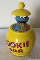 Front view showing yellow barrel jar, Cookie Monster figure, red lettering