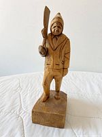 Front view of carved wooden man holding partial rifle on rectangular base