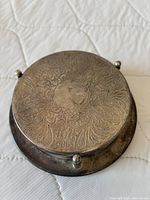 Top view of stacked silver-plated coasters in caddy showing chased baroque pattern and ball-foot pillars