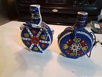 Front view of both blue leather-wrapped flasks showing decorative motifs
