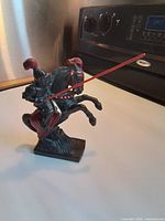 Front right view of the cast metal knight on rearing horse holding red lance