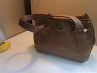 Front view of brown leather satchel showing handles, zipper, hardware and overall shape