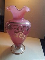 Full view of pink cased glass vase with gold scrollwork and clear foot