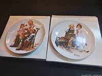 Both Norman Rockwell plates side by side on top of their original boxes