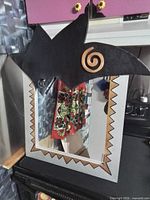 Full view of mirror showing grey and gold jagged frame, black topper with spiral, reflective glass