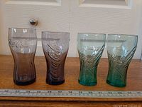 Front view of four Coca-Cola glasses—two purple, two teal—next to ruler