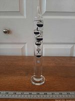 Full view of glass Galileo thermometer standing on wooden surface