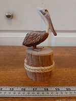 Front view of carved pelican on wooden piling base with rope, ruler for scale