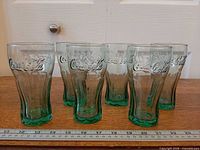 Front view of six green-tinted Libbey Coca-Cola tumblers lined up beside ruler
