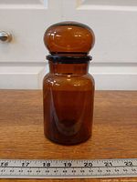 Full view of amber glass jar with stopper and ruler for scale