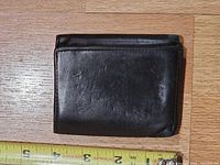 Front of closed black leather tri-fold wallet next to measuring tape showing size