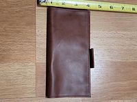 Front view of closed brown faux leather checkbook cover next to tape for scale