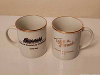 Front view of both mugs showing logos and gold rims