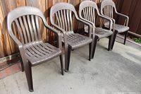 Four brown plastic patio chairs aligned against wood fence