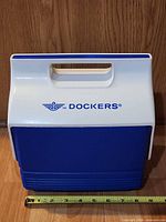 Front view of blue and white Dockers Igloo lunch cooler with handle down, measuring tape for width