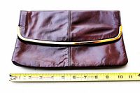 Front view of burgundy leather clutch with gold metal trim, tape measure showing width