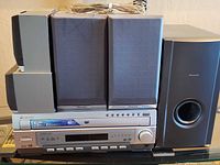 Front view of receiver, four satellites stacked, subwoofer; shows included speaker wires