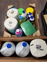 Two boxes of assorted cleaning products including bleach, paper towels and various bottles