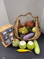 Faux fruit assortment in wicker basket beside small 6-drawer trinket box