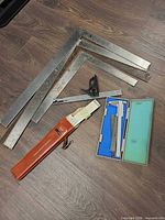 Group view of three large framing squares, combination square, engineer squares case, slide rule with case