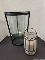 Large clear glass vase in metal stand beside frosted glass candle holder