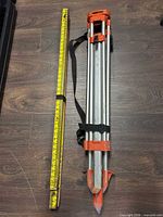 Collapsed aluminum survey tripod beside leveling rod