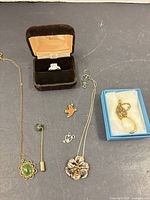 Overview of all six jewelry pieces including ring in box, jade necklace, jade tie pin, flower pendant necklace, bird pin, heart & anchor charm
