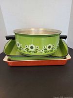 Three stacked items: green floral aluminum pot, green enamel pan, orange baking dish