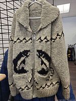 Front view of gray wool Cowichan-style sweater on hanger showing salmon motifs, zipper, pockets, shawl collar