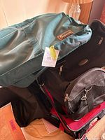 Overview of stacked green Amalfi duffel, black suitcase, black pet carrier and additional duffel