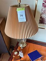 Lamp 1 showing clear glass body, brass base, beige pleated shade, harp and finial