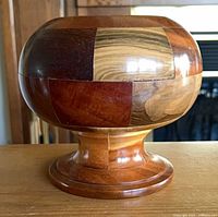 Side view of segmented wood decorative bowl on pedestal base showing varied wood tones and smooth finish