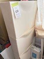 Front view of tall cream plastic IKEA cabinet with three drop-down drawers